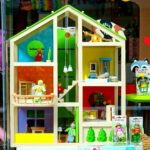 A vibrant dollhouse and stuffed toys displayed in a toy store window, perfect for children's play.